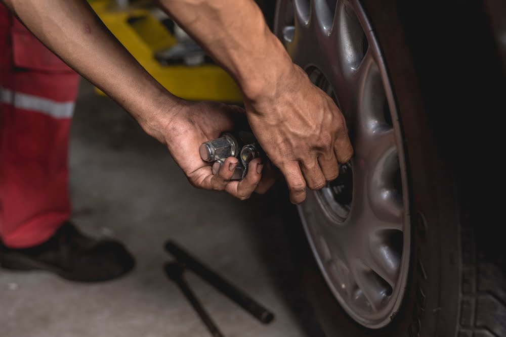 mechanic screws on lug nuts onto the tire of a serviced car